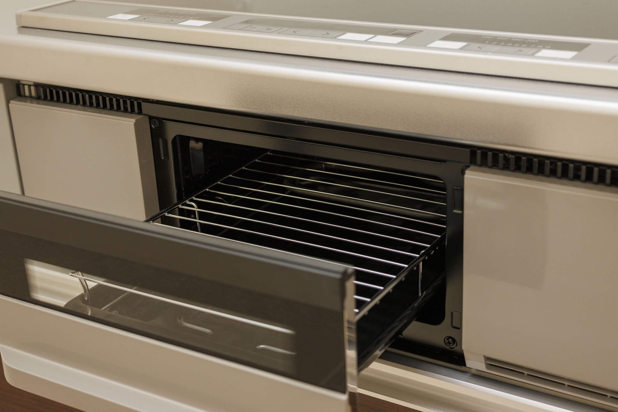 A modern kitchen oven with an open door reveals a clean metal rack inside. The control panel displays various cooking settings.