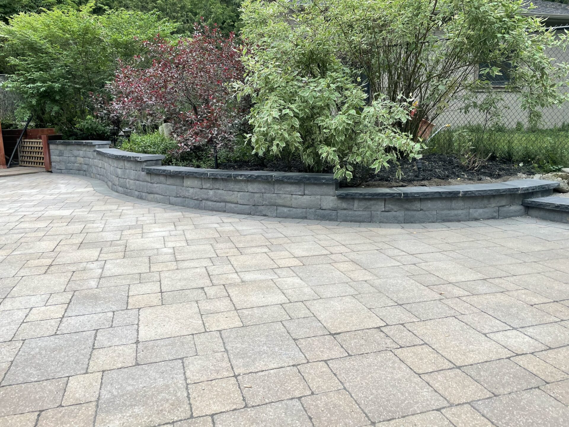A stone patio with a retaining wall around a garden.