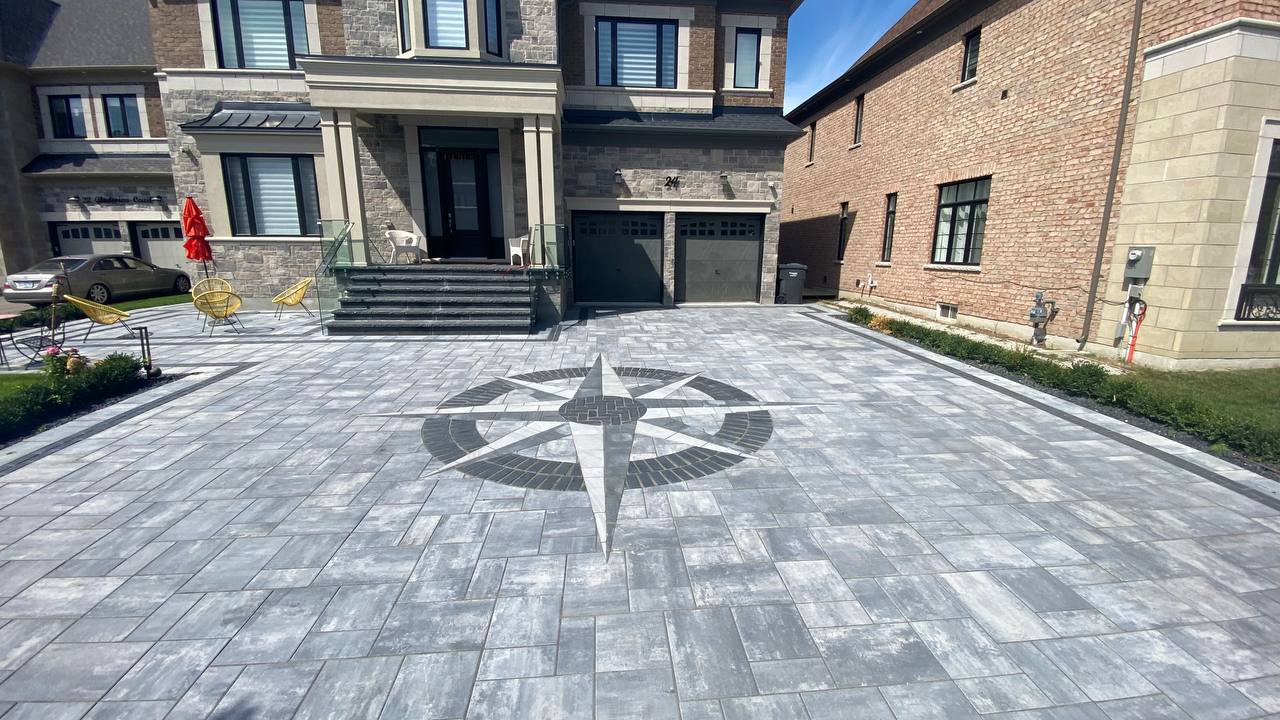 Modern house with a detailed compass design on the driveway. Patio features chairs and a red umbrella. Adjacent brick building visible.