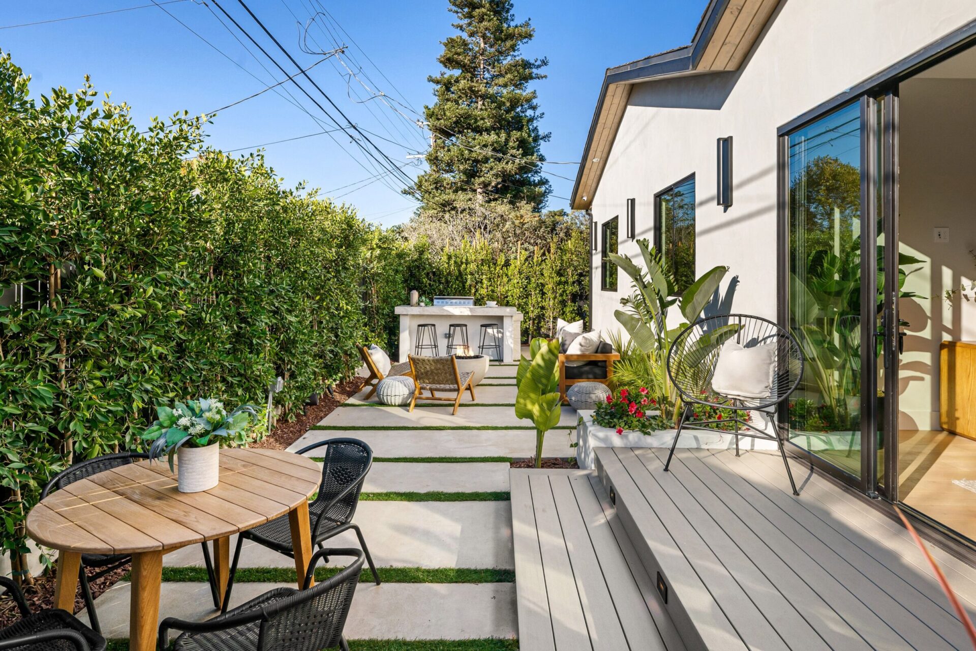 Modern backyard patio withlush greenery, outdoor seating, and a clear blue sky, ideal for relaxation and entertaining.