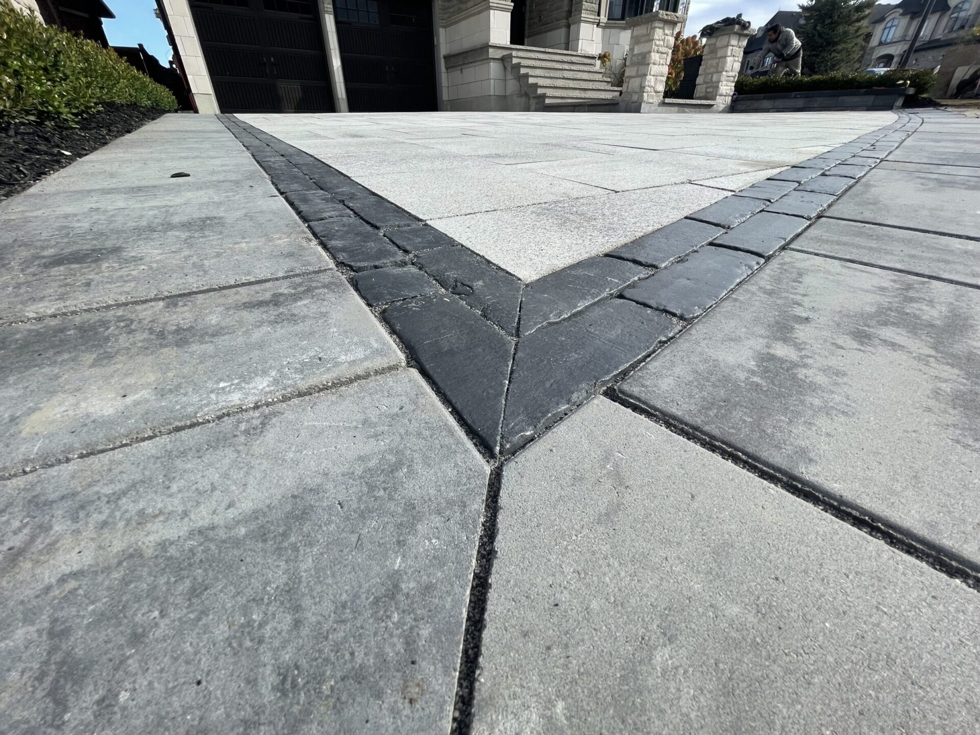 Close-up of a modern interlock driveway showing a precise V-shaped border pattern with dark and light gray pavers, highlighting clean lines and expert craftsmanship in residential hardscaping.