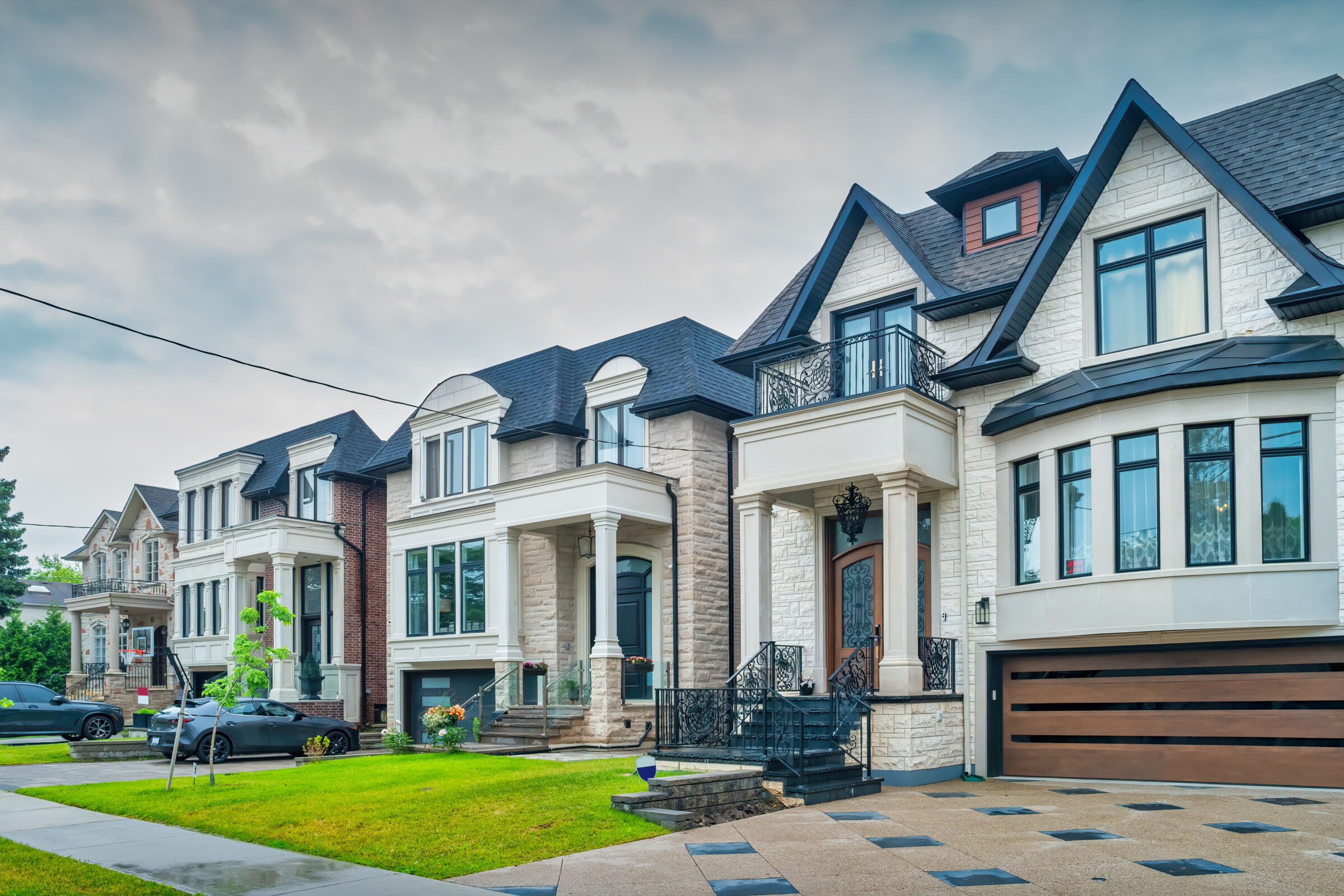 Row of luxury townhomes with elegant stone exteriors, large windows, and modern interlock driveways featuring a mix of concrete and dark stone inlay patterns on a cloudy day in a residential district in Toronto Ontario Canada.