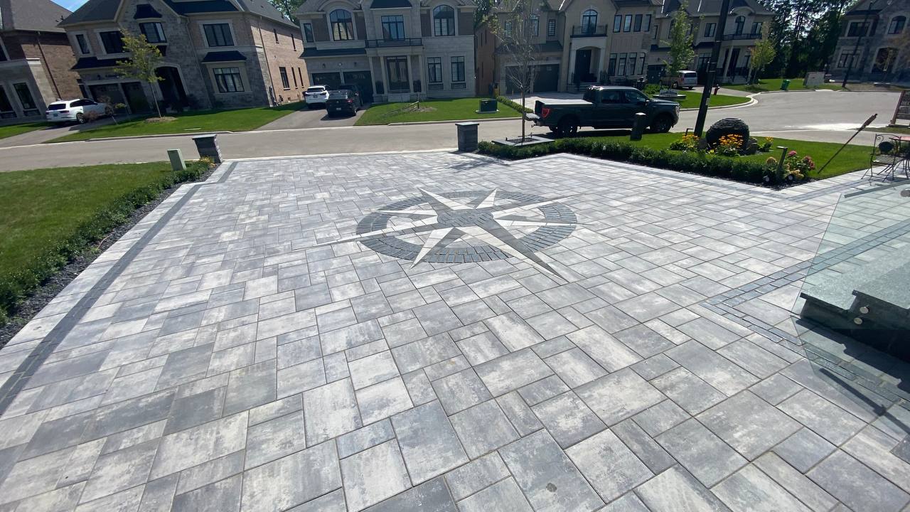 Freshly installed modern interlock driveway featuring light gray rectangular pavers with dark gray border accents, leading to a luxury stone-clad home with double garage and landscaped front yard.